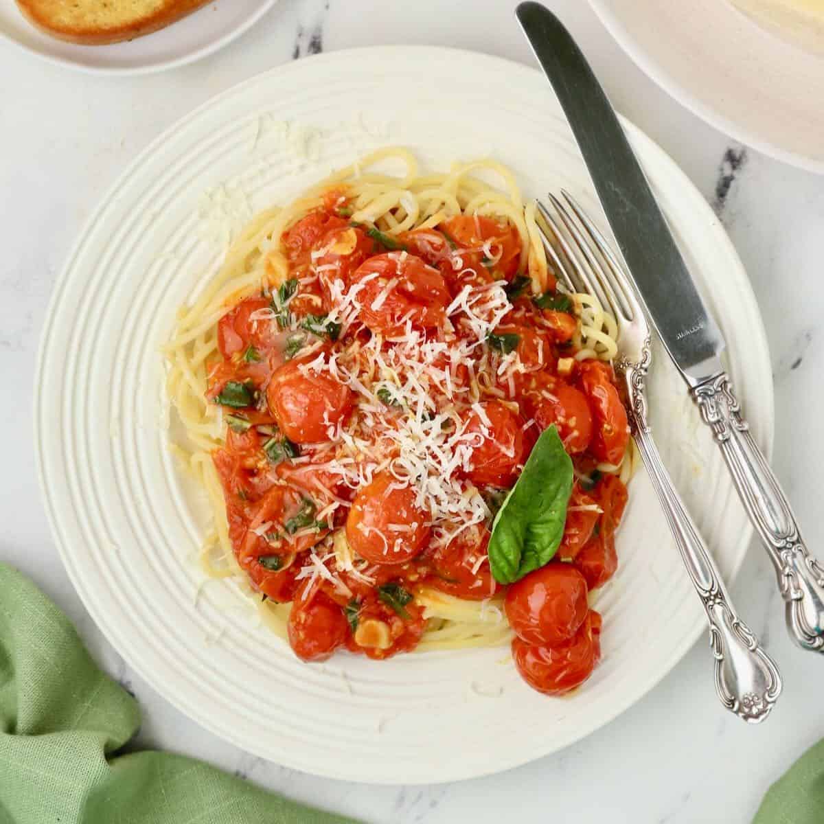 A plate full of spaghetti topped with Cherry Tomato Tomato Sauce and grated parmesan cheese.