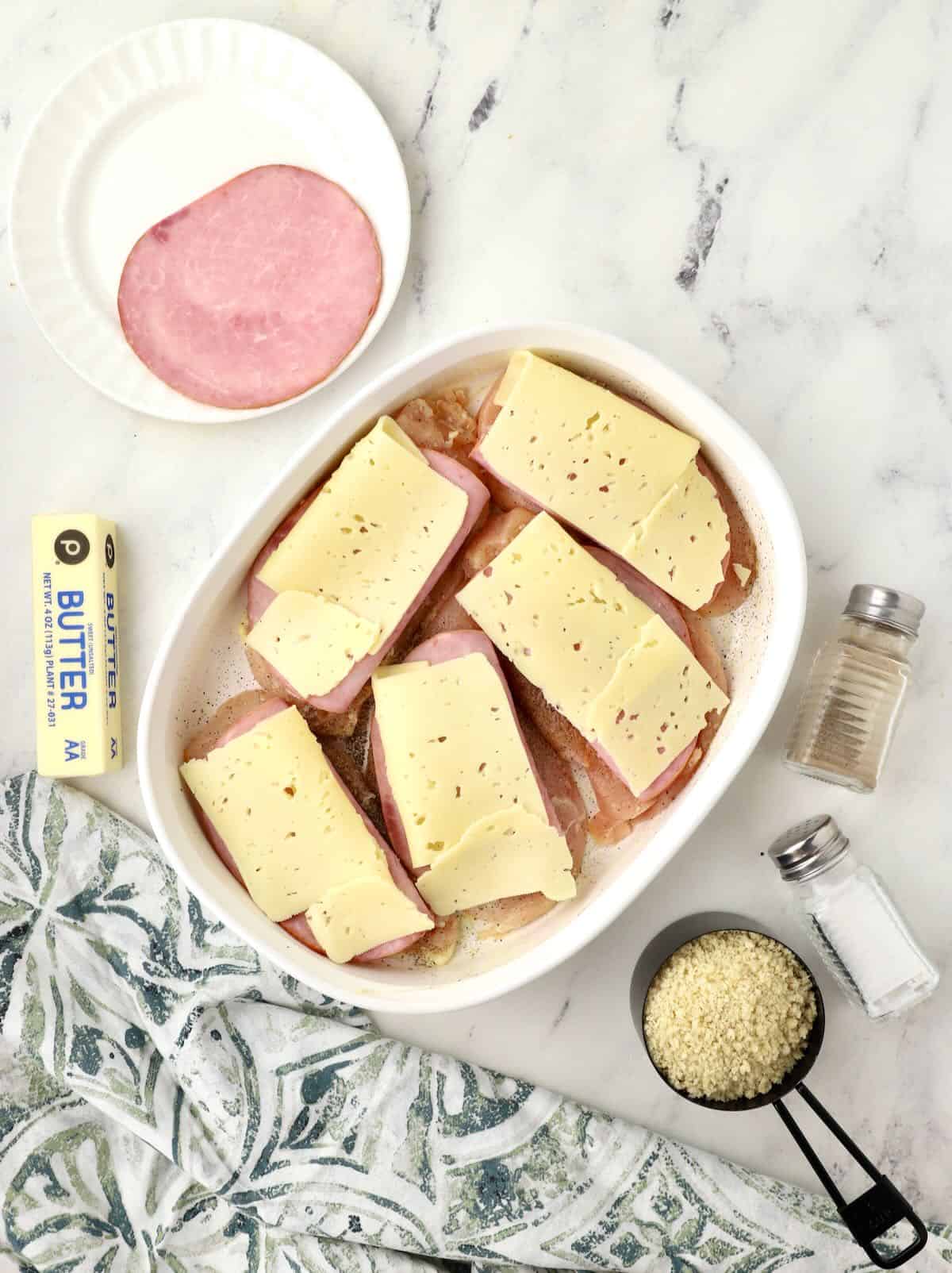 Chicken cutlets in a baking dish topped with ham and swiss cheese. 