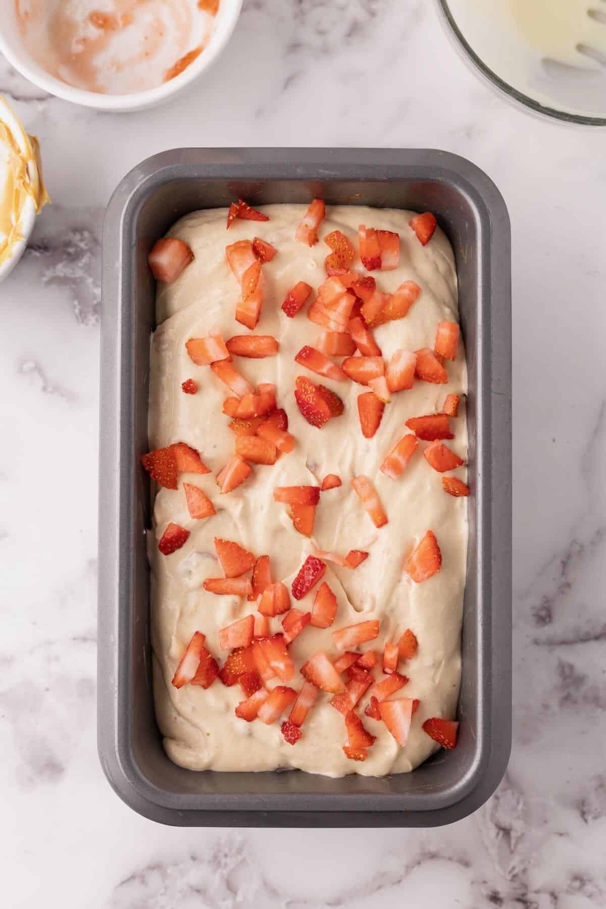 A loaf pan full of ice cream topped with chopped strawberries. 