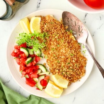 A baked snapper fillet topped with panko on a white plate with lemons for garnish.