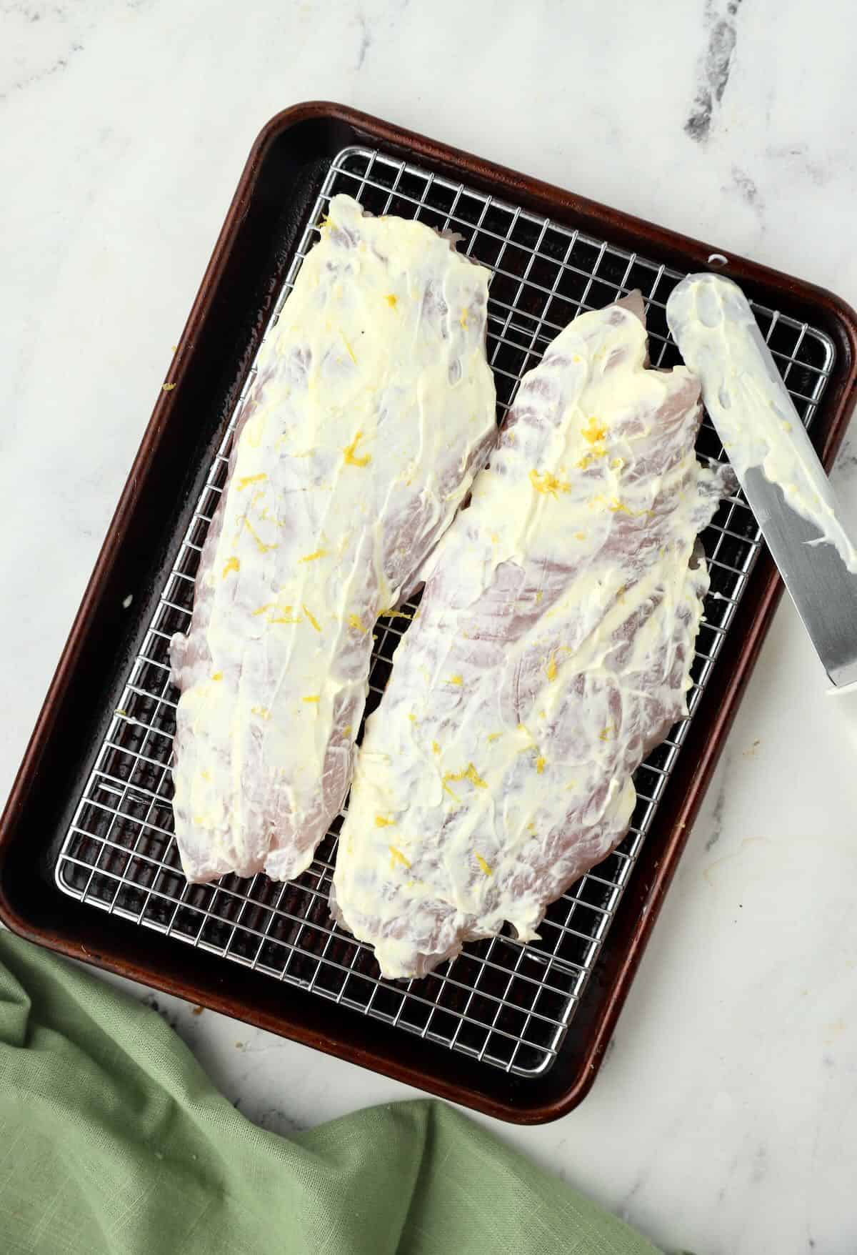 Two snapper fillets topped with mayonnaise and lemon zest.