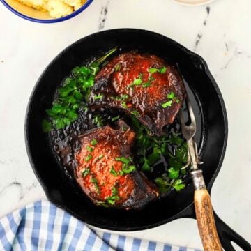 Two blackened pork chops in a cast iron skillet garnished with parsley.