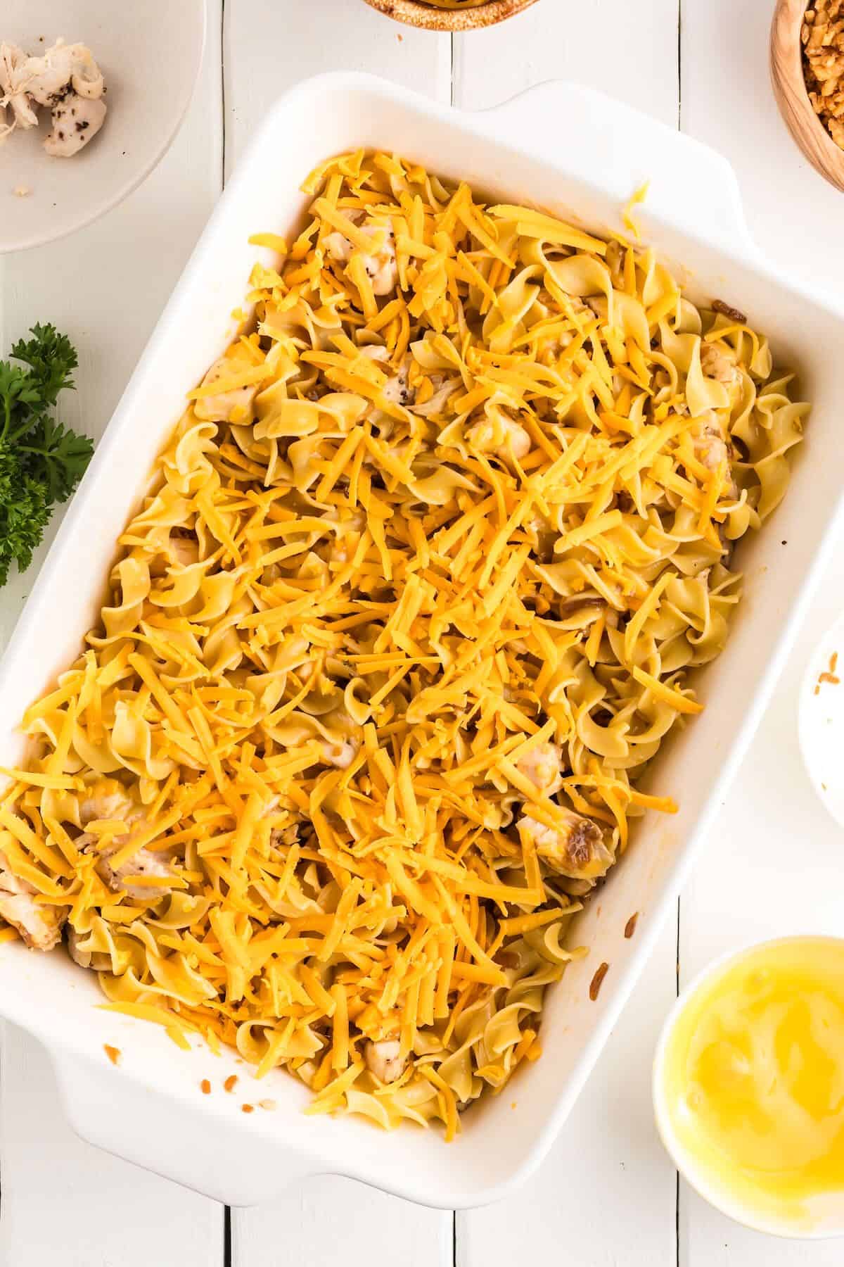 A baking dish full of egg noodles topped with shredded cheese.