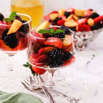 Fruit salad cocktail with cut-up fruit and berries in a glass dessert serving dish.