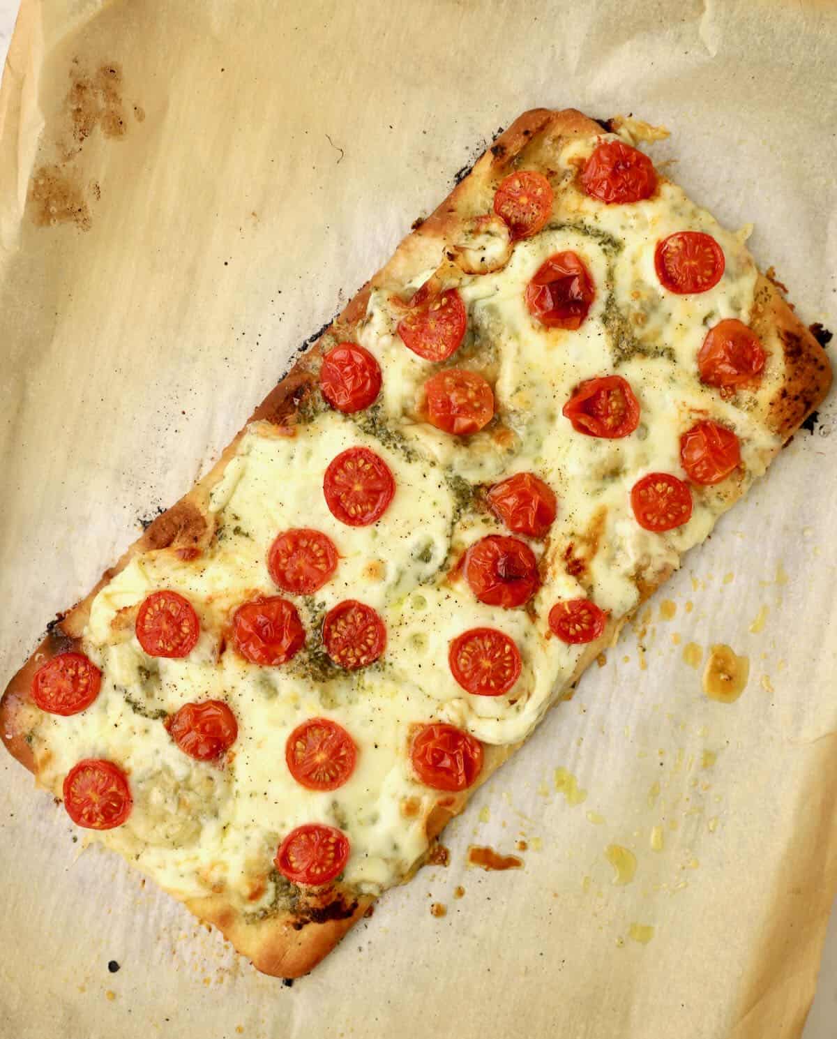 Baked caprese flatbread topped with melted mozzarella cheese and cherry tomatoes. 
