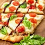Caprese flatbread sliced on a cutting board garnished with fresh basil.