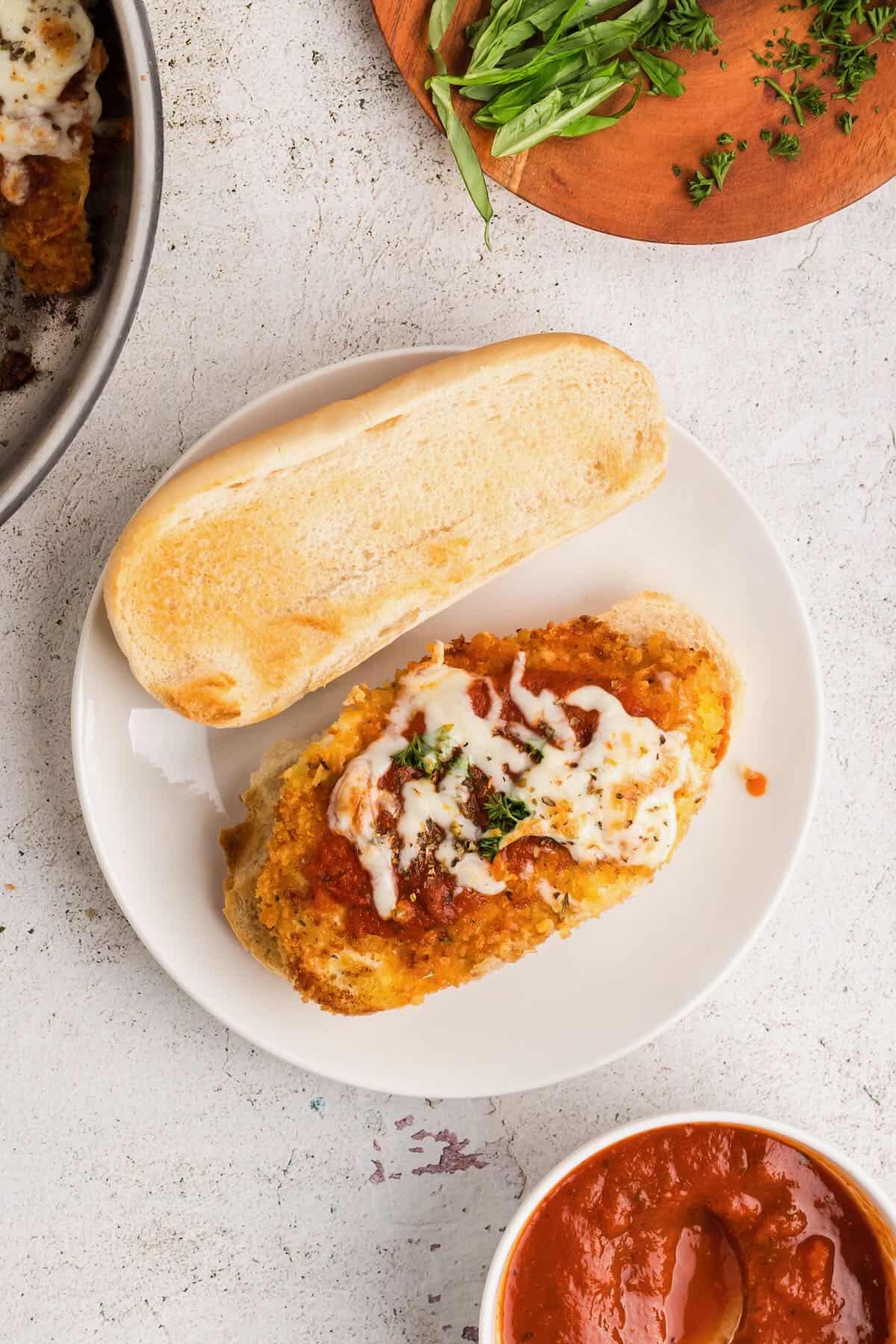 A toasted hoagie roll with a piece of fried chicken topped with marinara sauce and melted mozzarella cheese. 