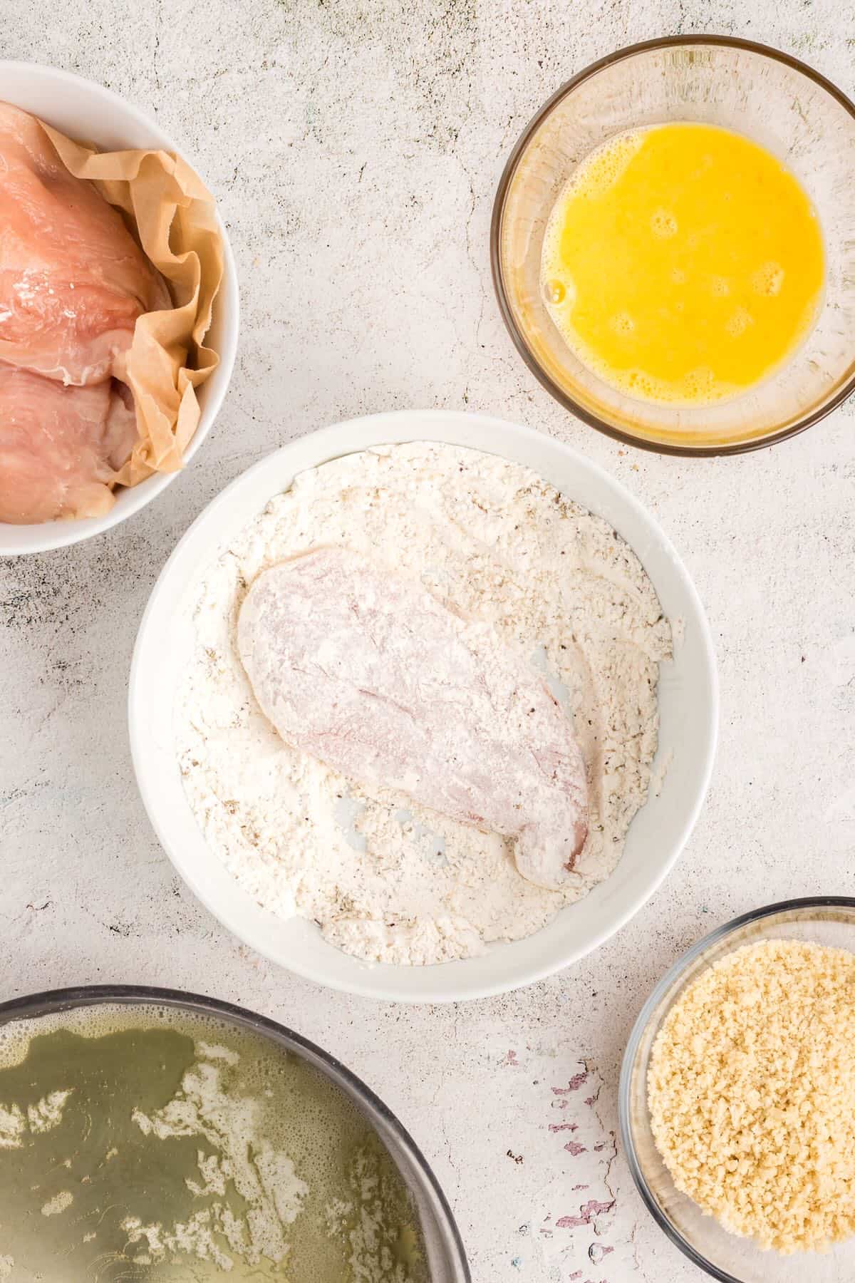 A chicken breast is dredged in a flour mixture. 