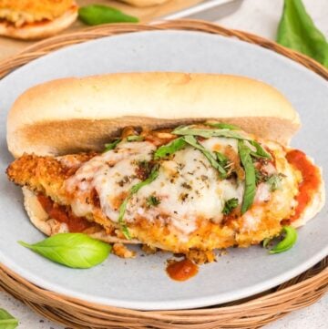 A chicken parmesan sandwich on a gray plate garnished with fresh basil.