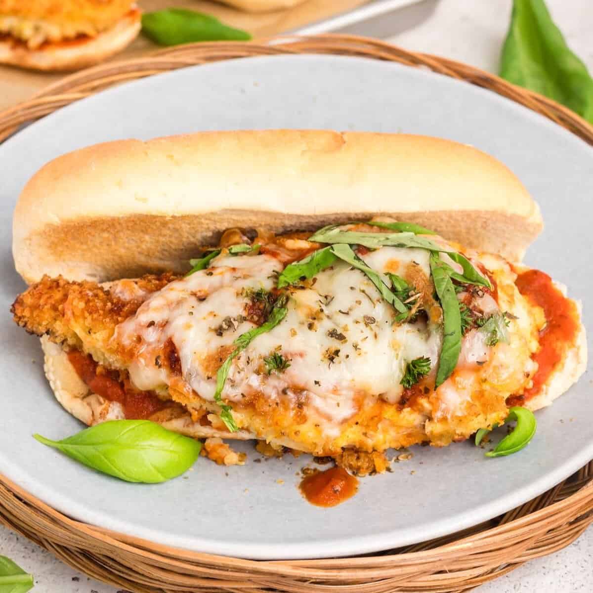A chicken parmesan sandwich on a gray plate garnished with fresh basil.