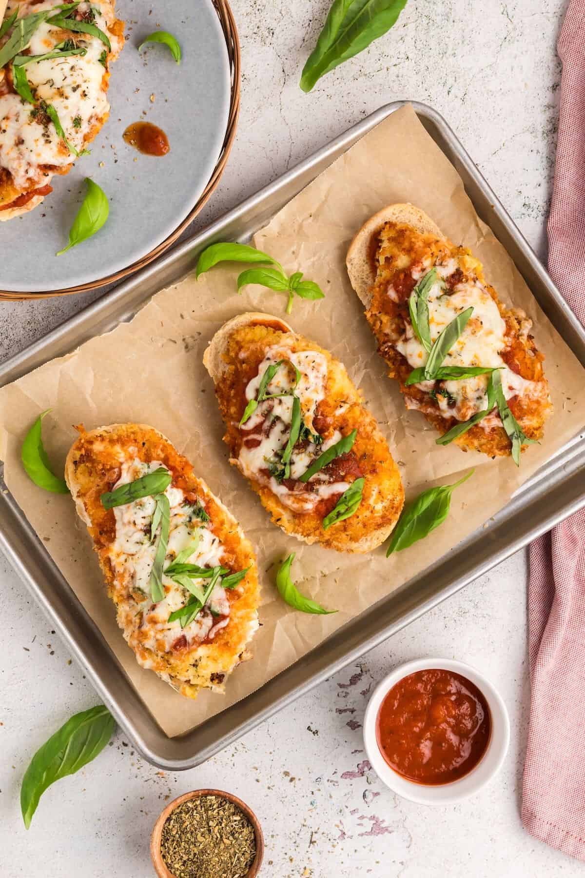 A baking sheet with three chicken parmesan sandwiches.