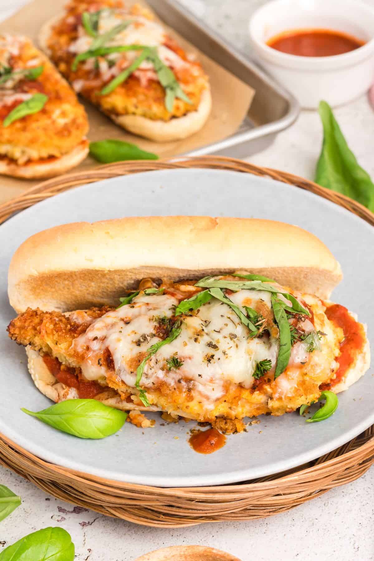 A chicken parmesan sandwich on a gray plate garnished with basil. 