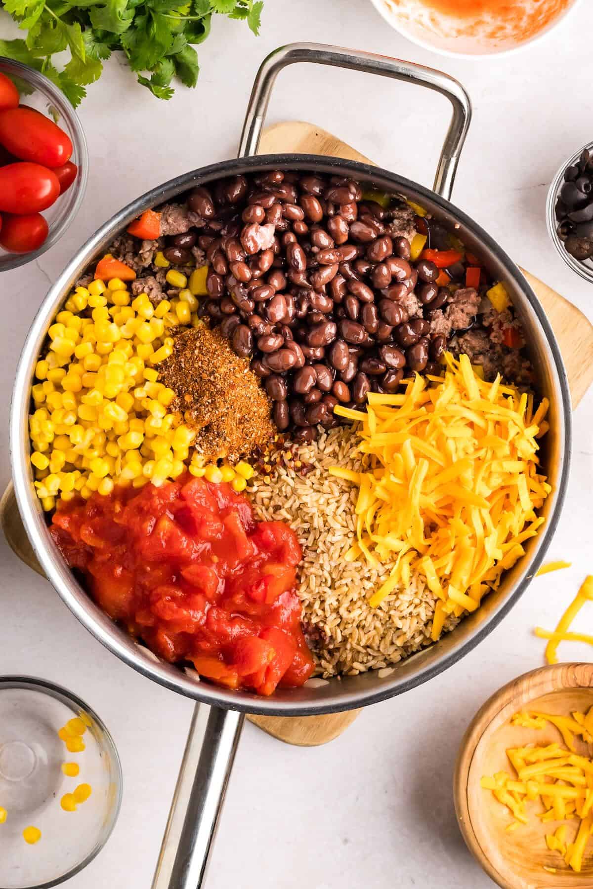 A large skillet with black beans, canned tomatoes, corn, rice and cheese added. 