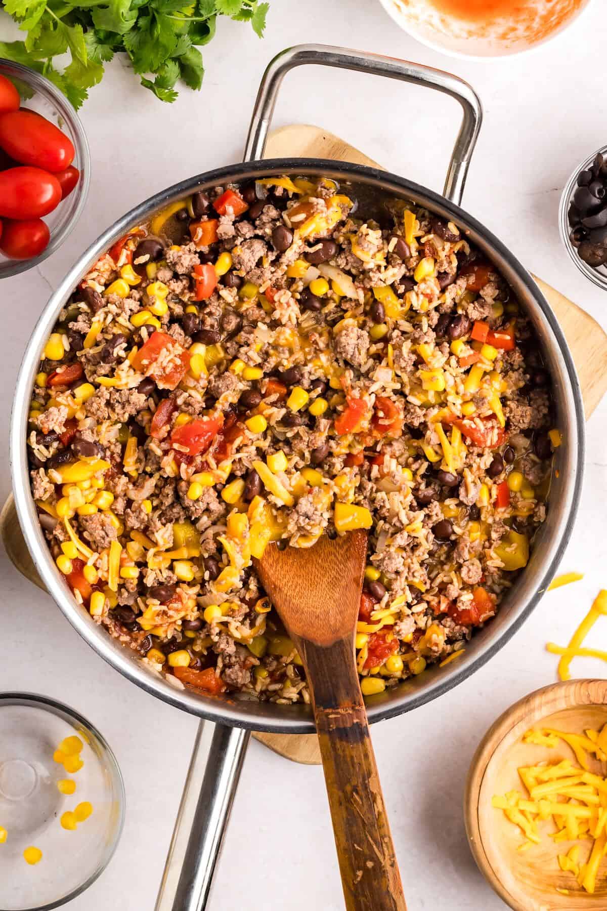 A large skillet full of cooked ground beef, peppers, onions, corn, beans and cheese. 
