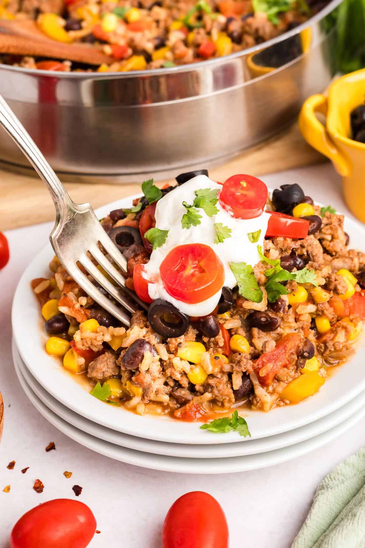 A serving of Mexican Beef Rice Skillet on a white plate topped with sour cream and tomato slices. 