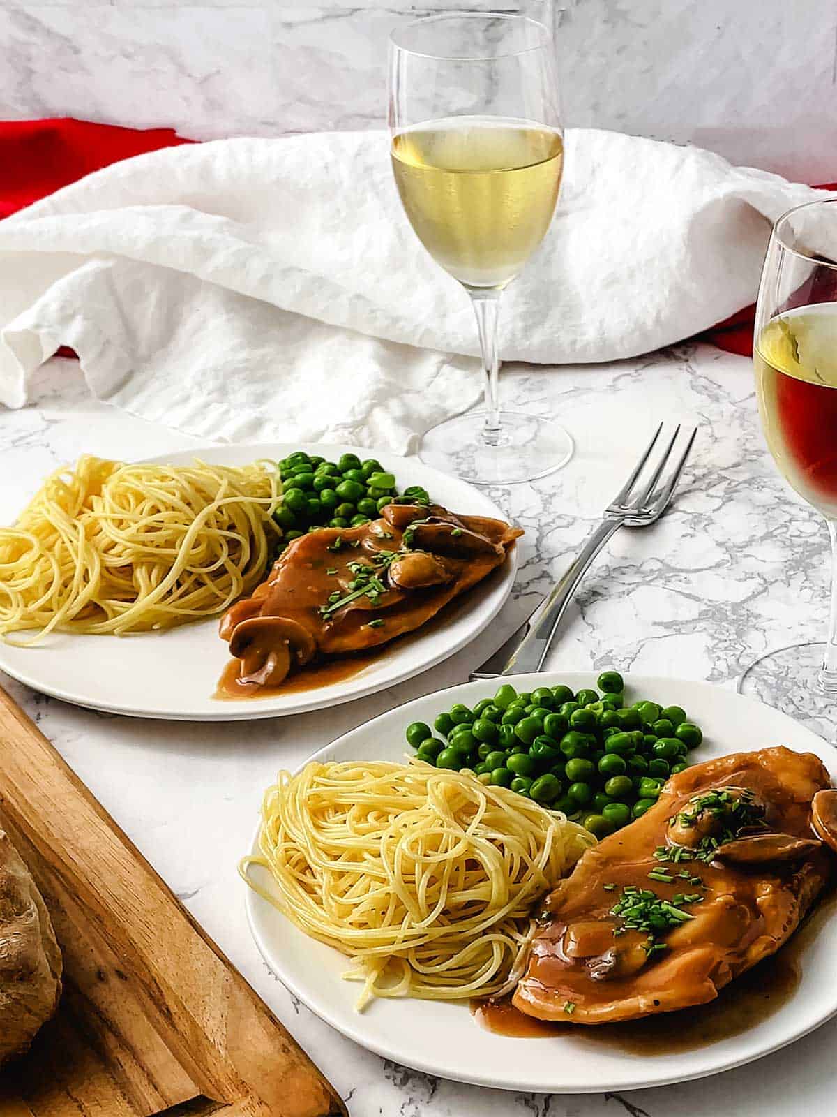 Two white plates with chicken scallopini topped with mushrooms and gravy.