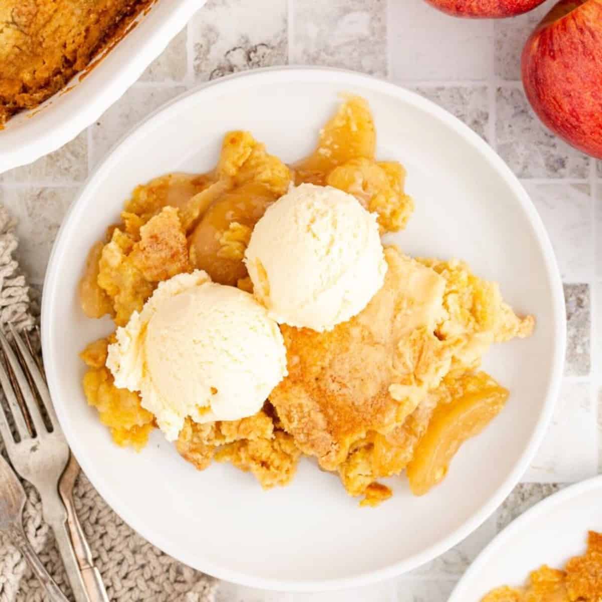 A serving of apple cobbler with cake mix topped with two scoops of vanilla ice cream.