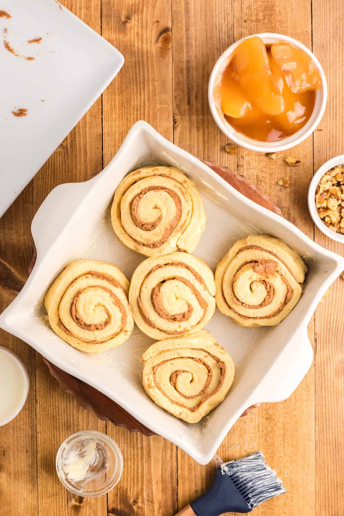 Five unbaked cinnamon rolls in a square baking dish. 