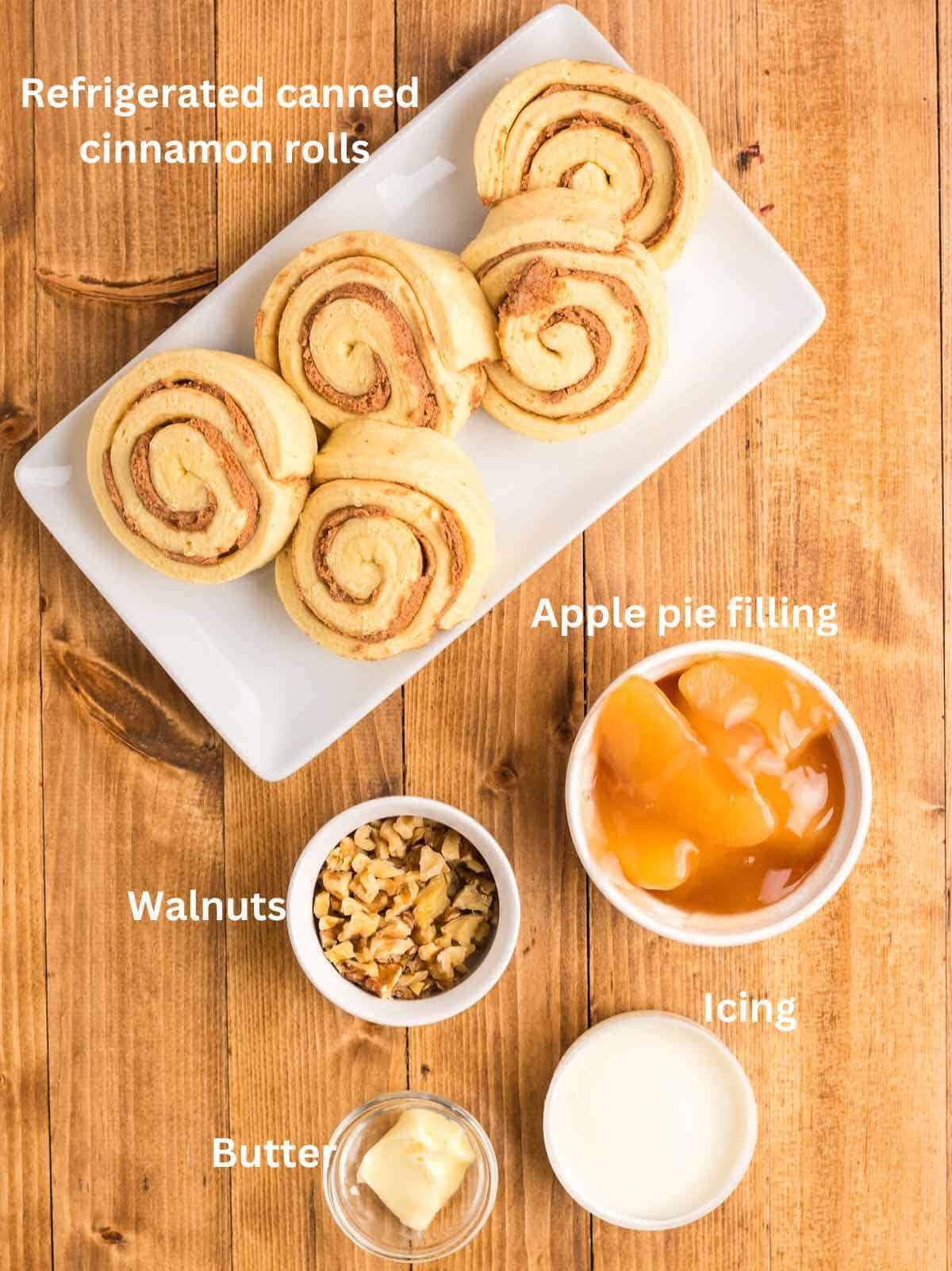 Ingredients for apple pie cinnamon rolls including refrigerated canned cinnamon rolls, apple pie filling, nuts, and icing. 