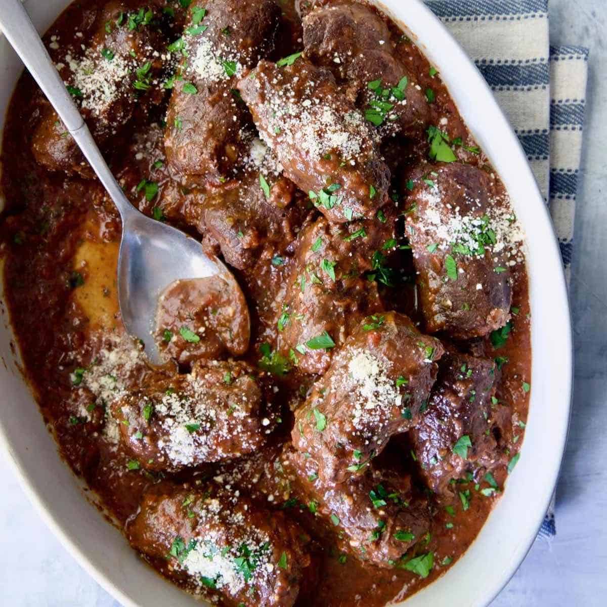 Beef Braciole in a white serving dish topped with parmesan cheese. 