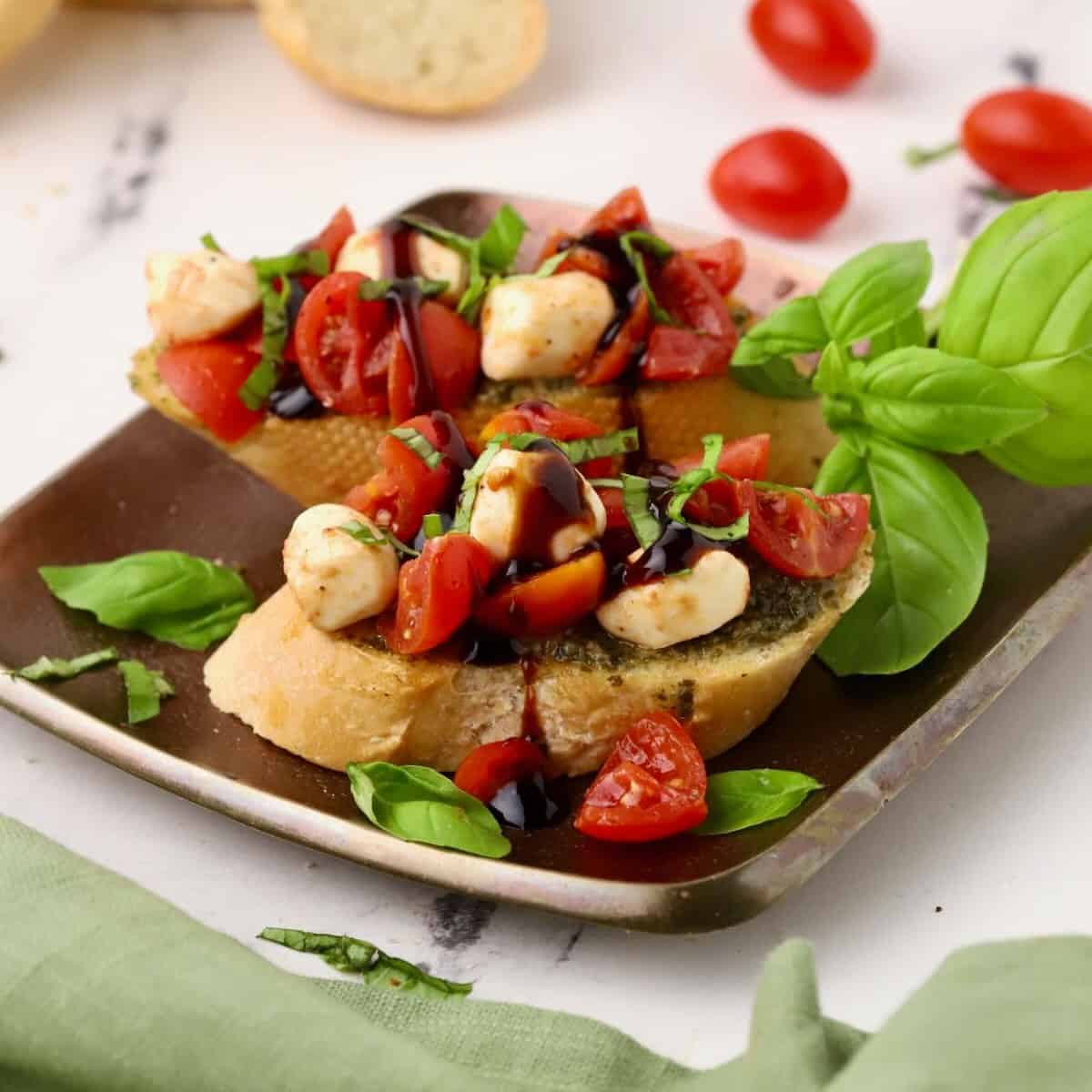 Caprese Bruschetta is a Caprese salad on toast with pesto topped with basil.