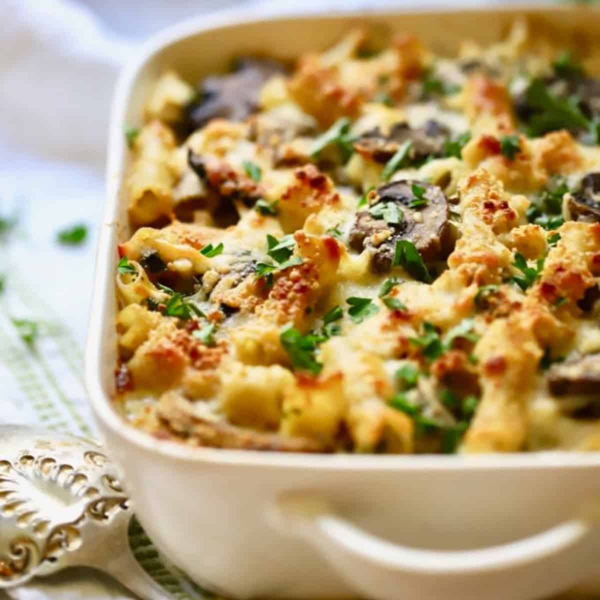 A white baking dish full of chicken marsala pasta topped with chopped parsley. 