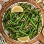 A plate full of garlic parmesan green beans topped with parmesan cheese and garnished with slices of lemon.