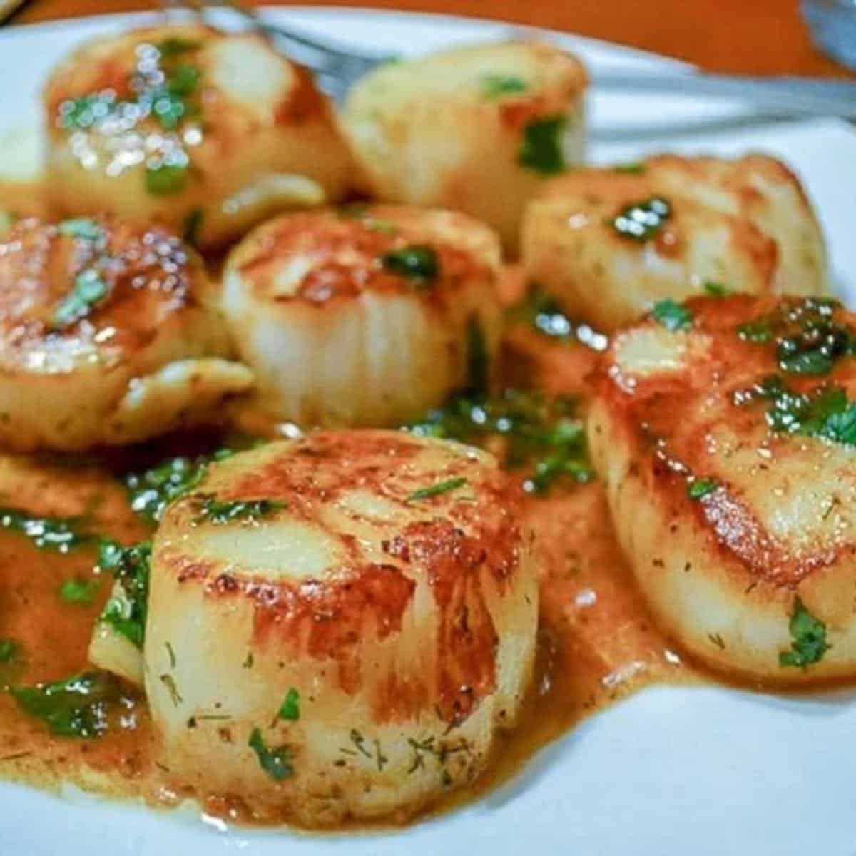 Pan seared scallops on a plate topped with brown butter. 