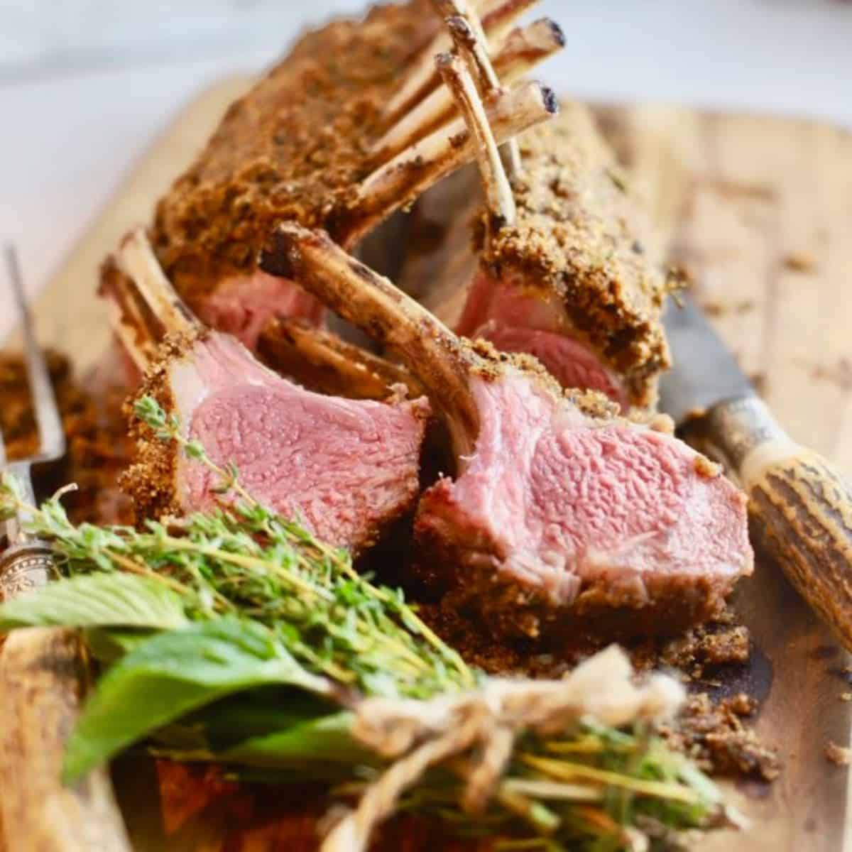 Sliced rack of lamb with a bundle of herbs on a cutting board. 