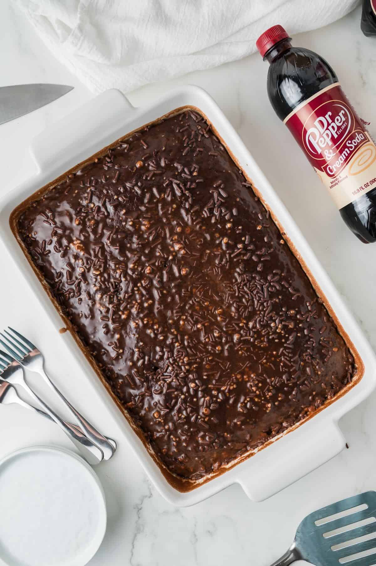 Dr Pepper chocolate sheet cake topped with chocolate icing in a white baking dish. 