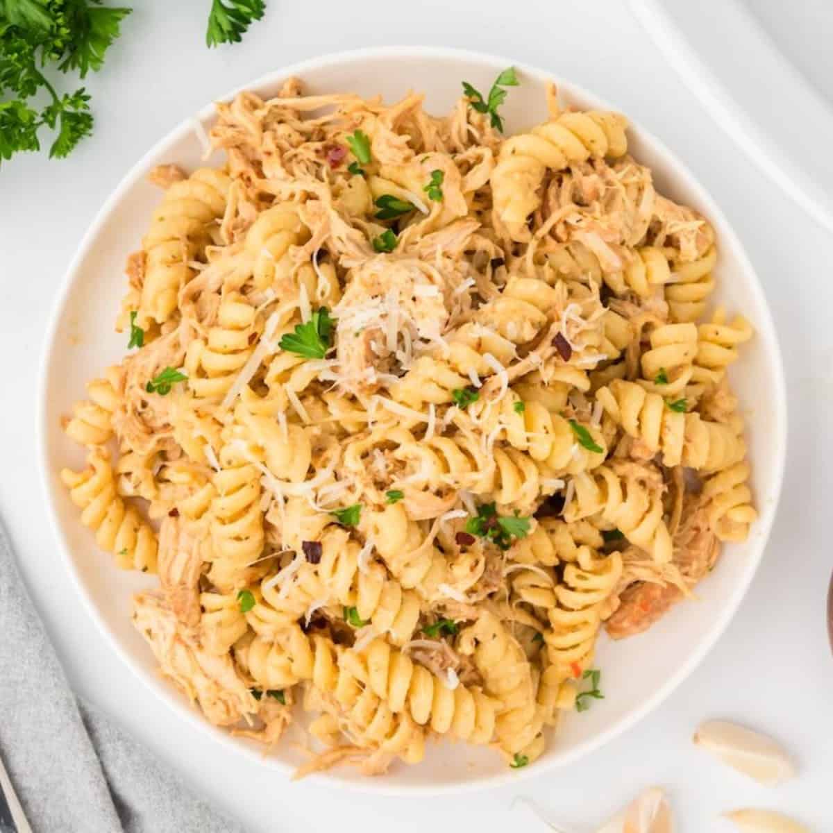 A white plate full of crock pot garlic parmesan chicken pasta garnished with parsley.