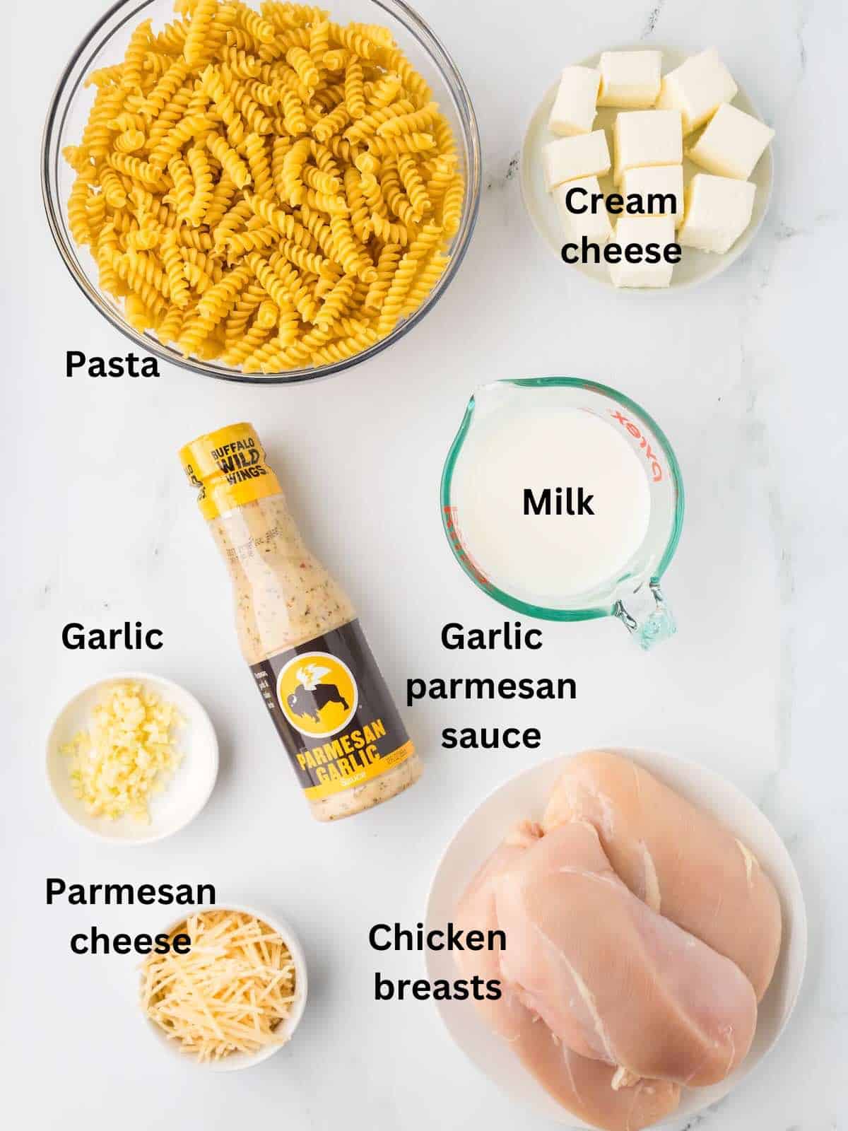 A bowl of pasta, chicken breasts, parmesan cheese, cream cheese, and a cup of milk. 