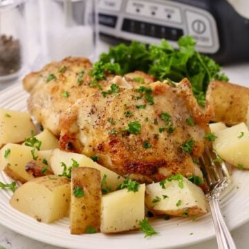 Two pieces of crockpot crispy chicken on a plate with cubed potatoes.
