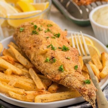 A fried whole catfish on a plate with french fries and a fork.