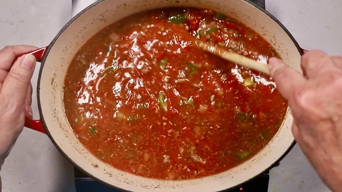 Lasagna soup ingredients in a large pot including ground beef, tomato sauce and diced tomatoes. 