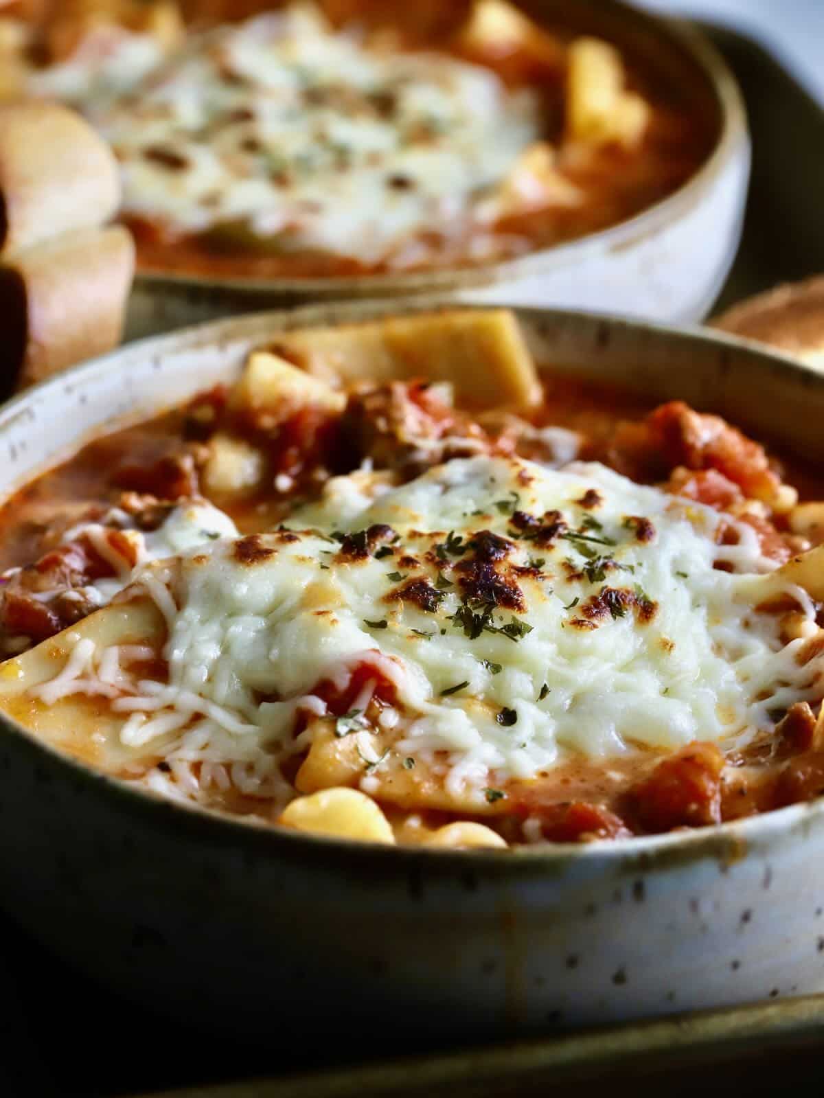 A bowl of lasagna soup with melted mozzarella cheese on top.