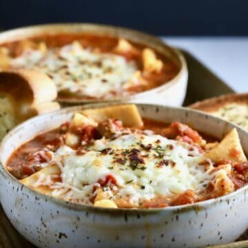 Two bowls full of lasagna soup with melted cheese on top.
