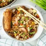 Shrimp and chicken fried rice in a white bowl with chopsticks and an egg roll.