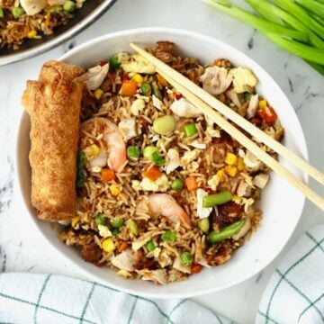Shrimp and chicken fried rice in a white bowl with chopsticks and an egg roll.