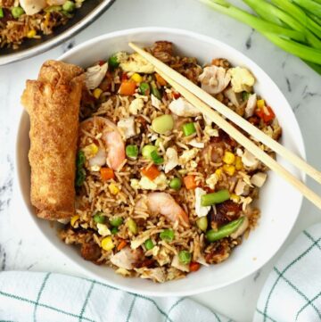 Chicken and shrimp fried rice in a white bowl with chopsticks and an egg roll.
