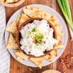 Bacon cream cheese dip on a plate with crackers and garnished with pecans and chopped-up scallions.