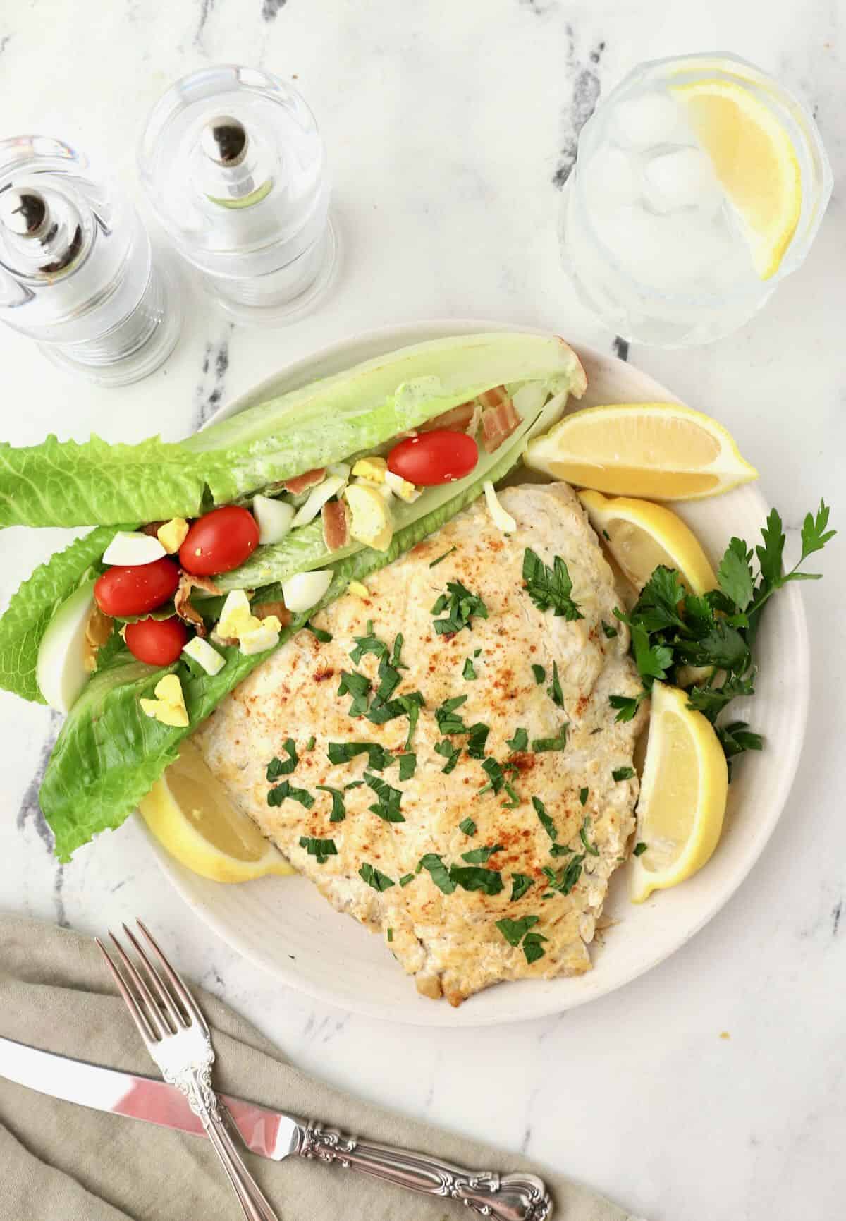 A baked grouper fillet topped with sour cream and paprika on a plate with a salad. 
