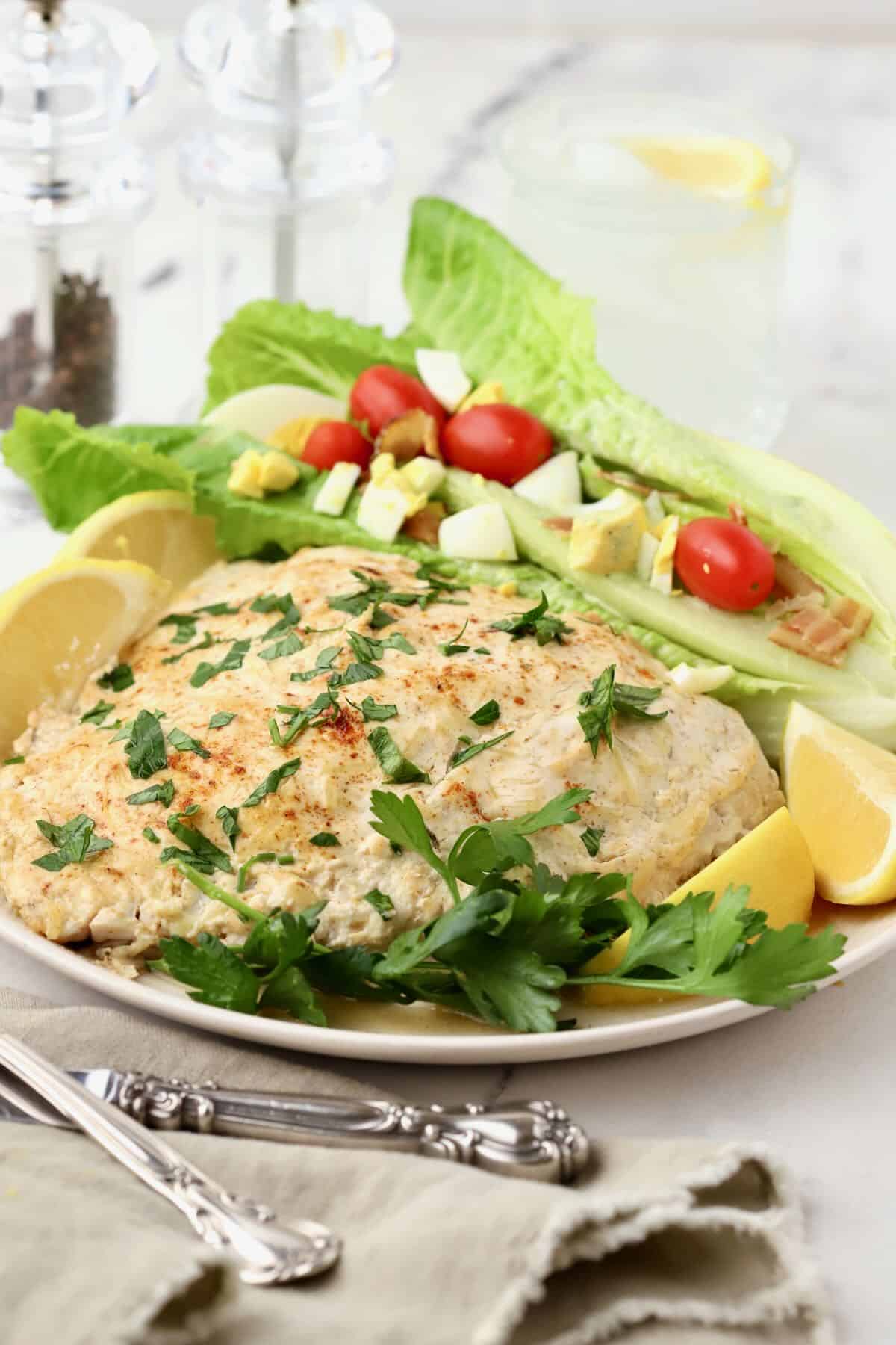 A large baked parmesan grouper fillet on a plate with a salad.