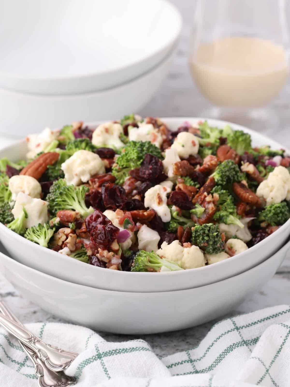 Broccoli, cauliflower, cranberry salad topped with pecans in a white serving bowl. 