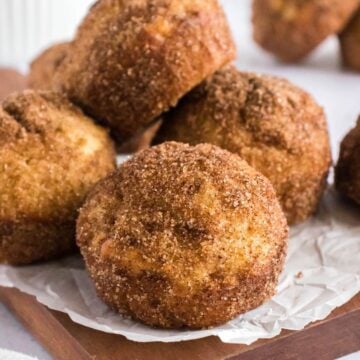 several cinnamon muffins on a wooden cutting board.