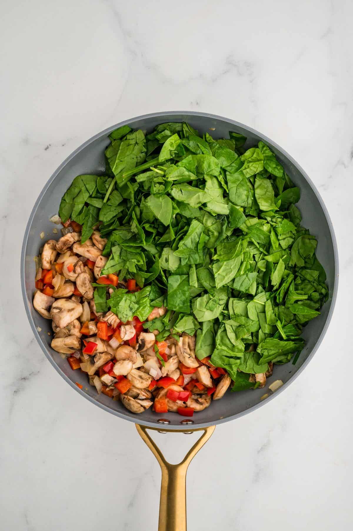 Sauteeing veggies incuding spinach and mushrooms in a skillet. 