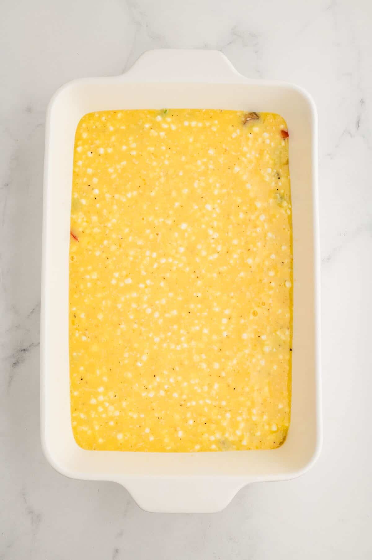 A white casserole baking dish full of veggies and an egg and cottage cheese mixture. 