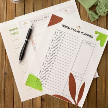 Three meal planner guides on a cutting board with a pen.