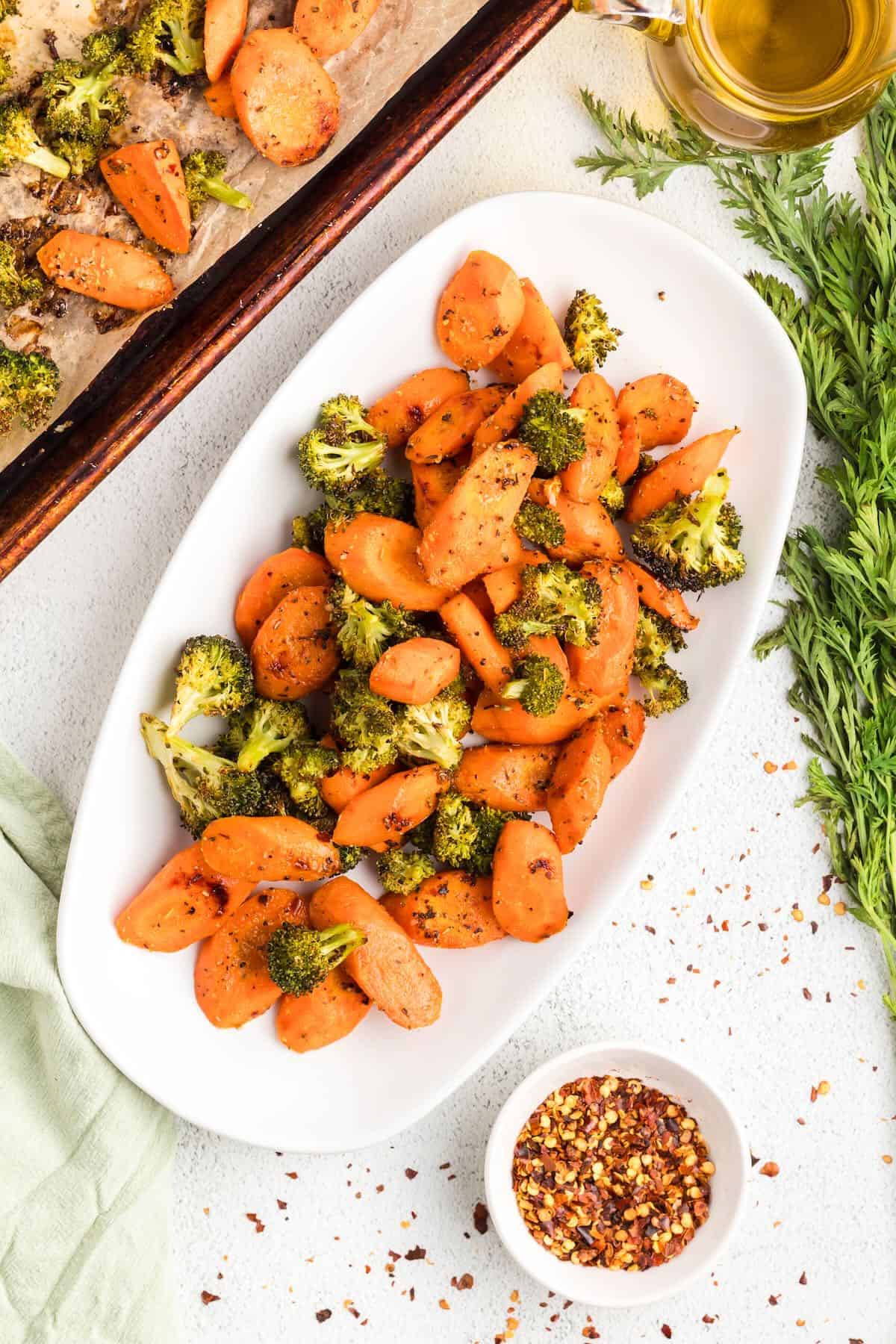 Roasted broccoli and carrots on a white oval bowl on a table.