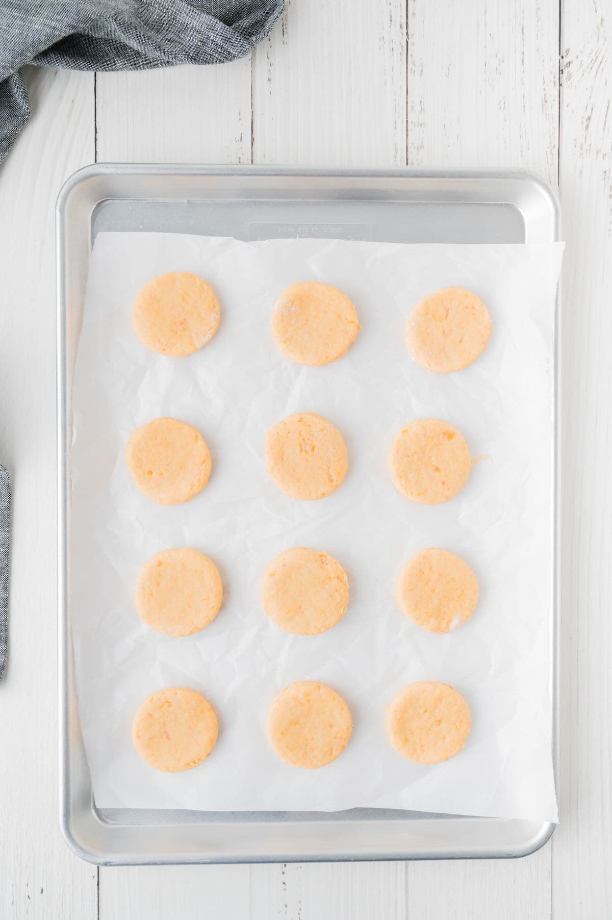 Biscuit dough rounds placed on parchment paper on a baking sheet. 